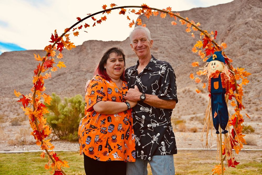 Smiling couple posing together under a circular autumn leaf arch with a scarecrow in the desert.