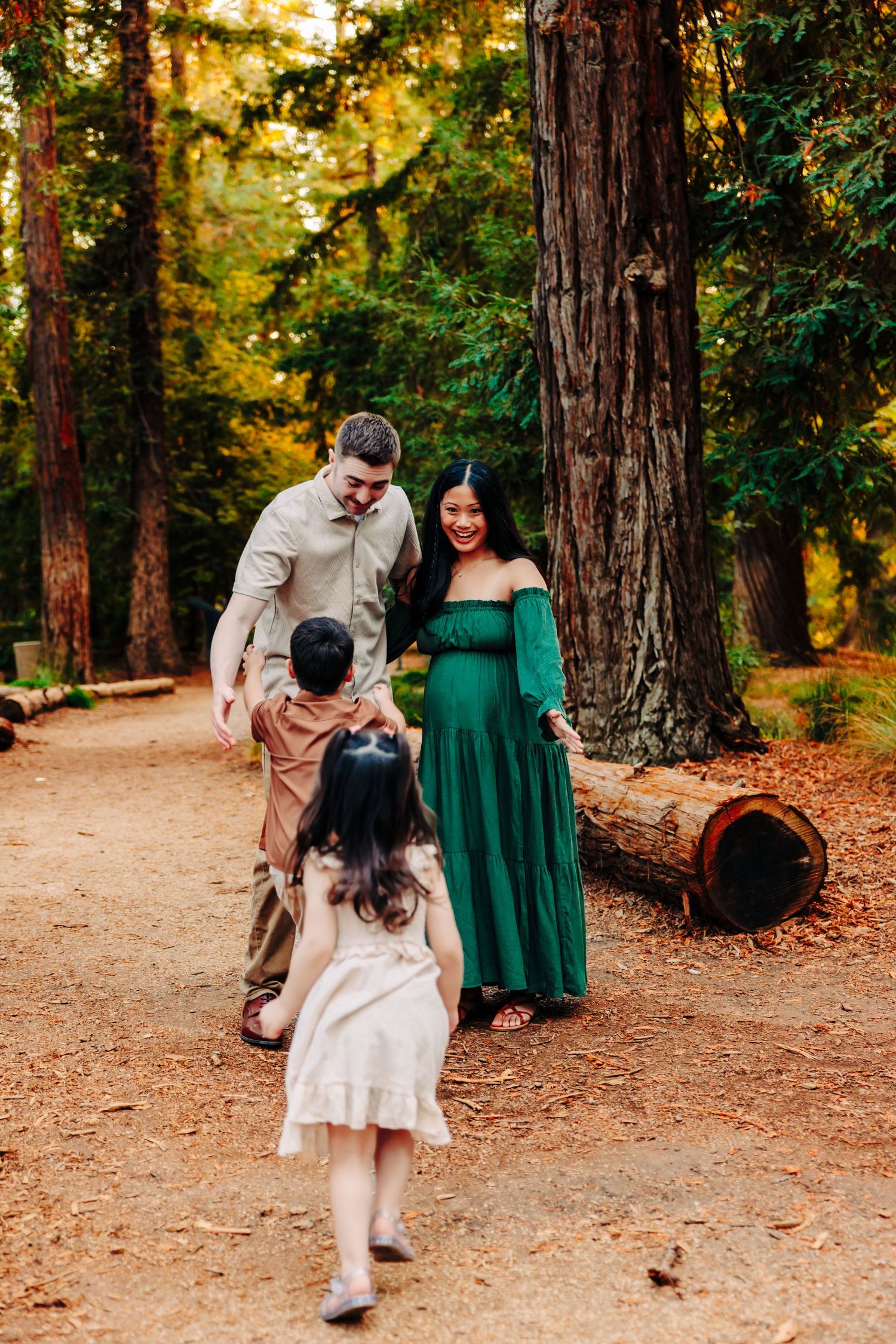 A family plays together on a forest trail surrounded by tall trees and autumn foliage.
