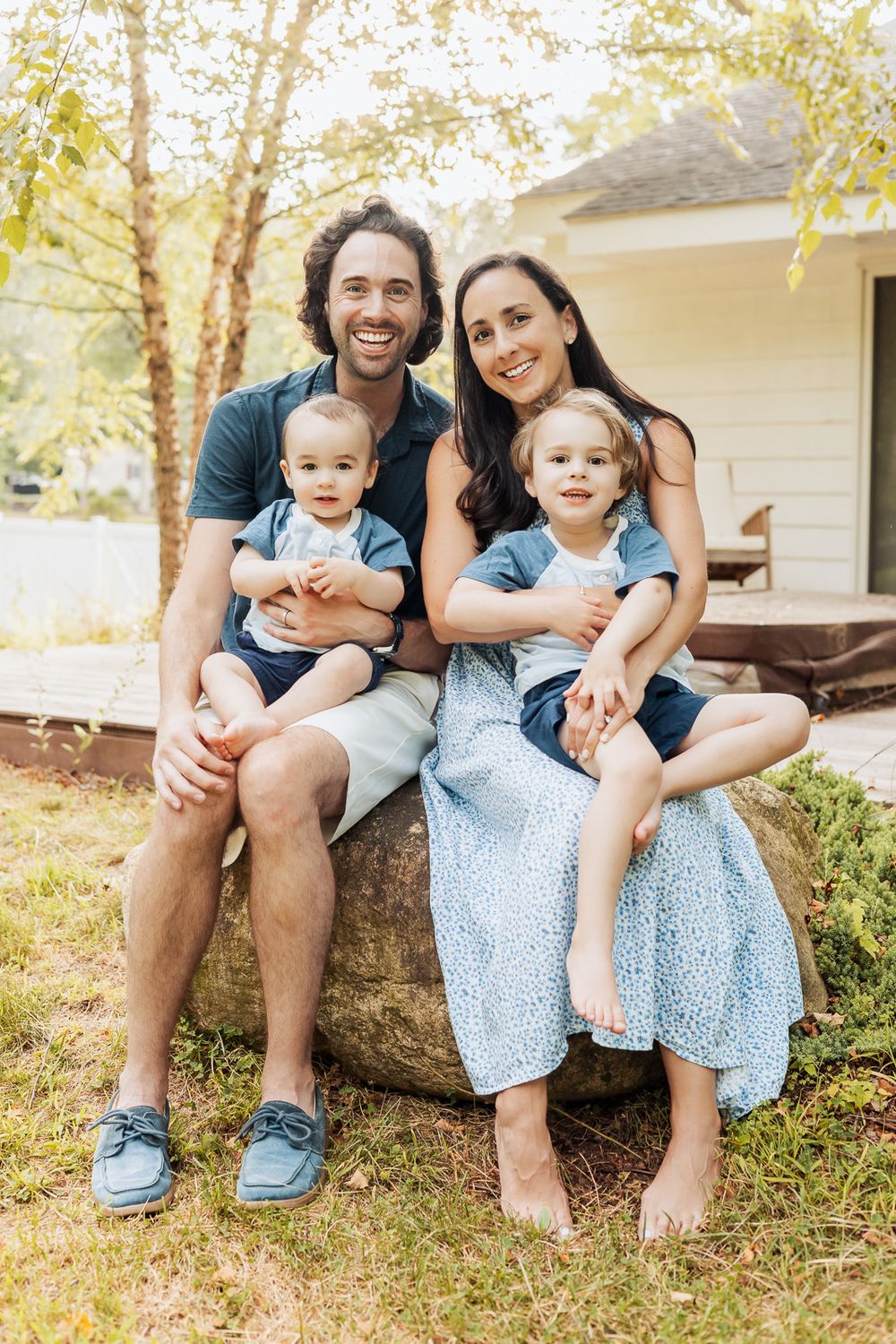 Family members sit casually on outdoor stone steps wearing coordinated blue outfits on a sunny day.