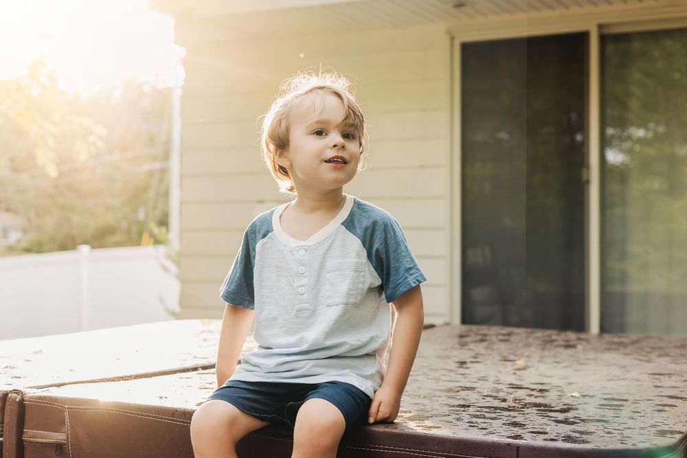 Young child sitting on wooden deck steps during golden hour sunlight creating a warm, nostalgic outdoor scene.