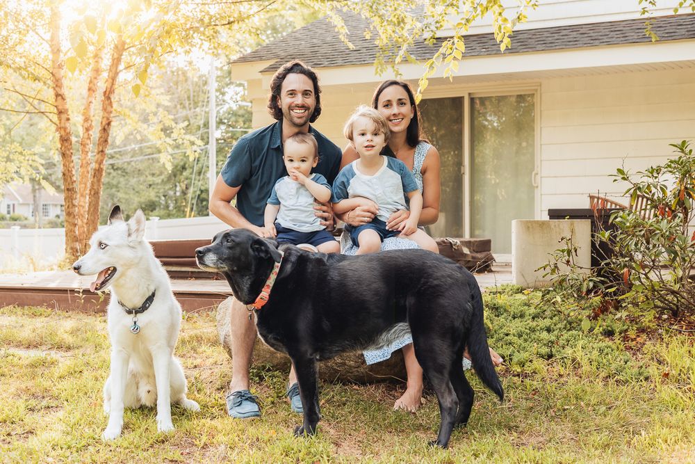 A family and their dogs sit together on stone steps in a sunlit backyard garden setting.