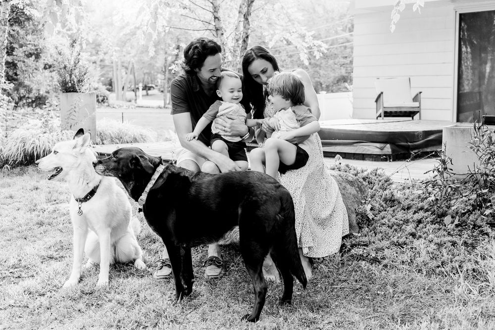 A black and white photo of a family sitting outdoors with their two dogs in a backyard setting.