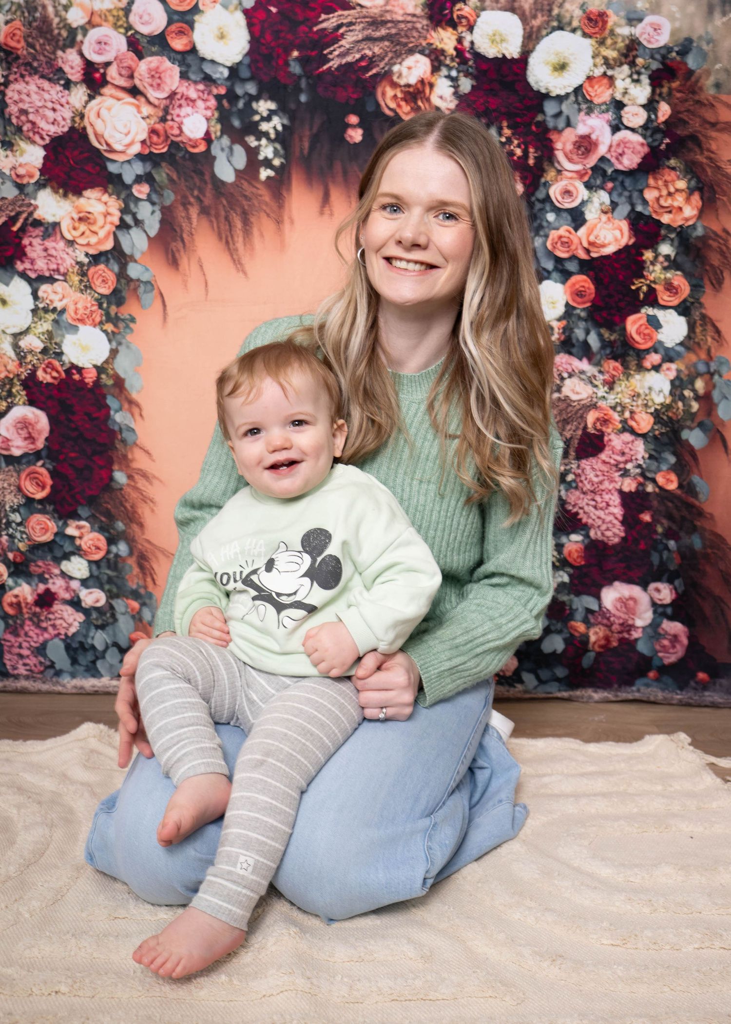 A floral backdrop with pink and peach roses creates a romantic setting for a family photo session.