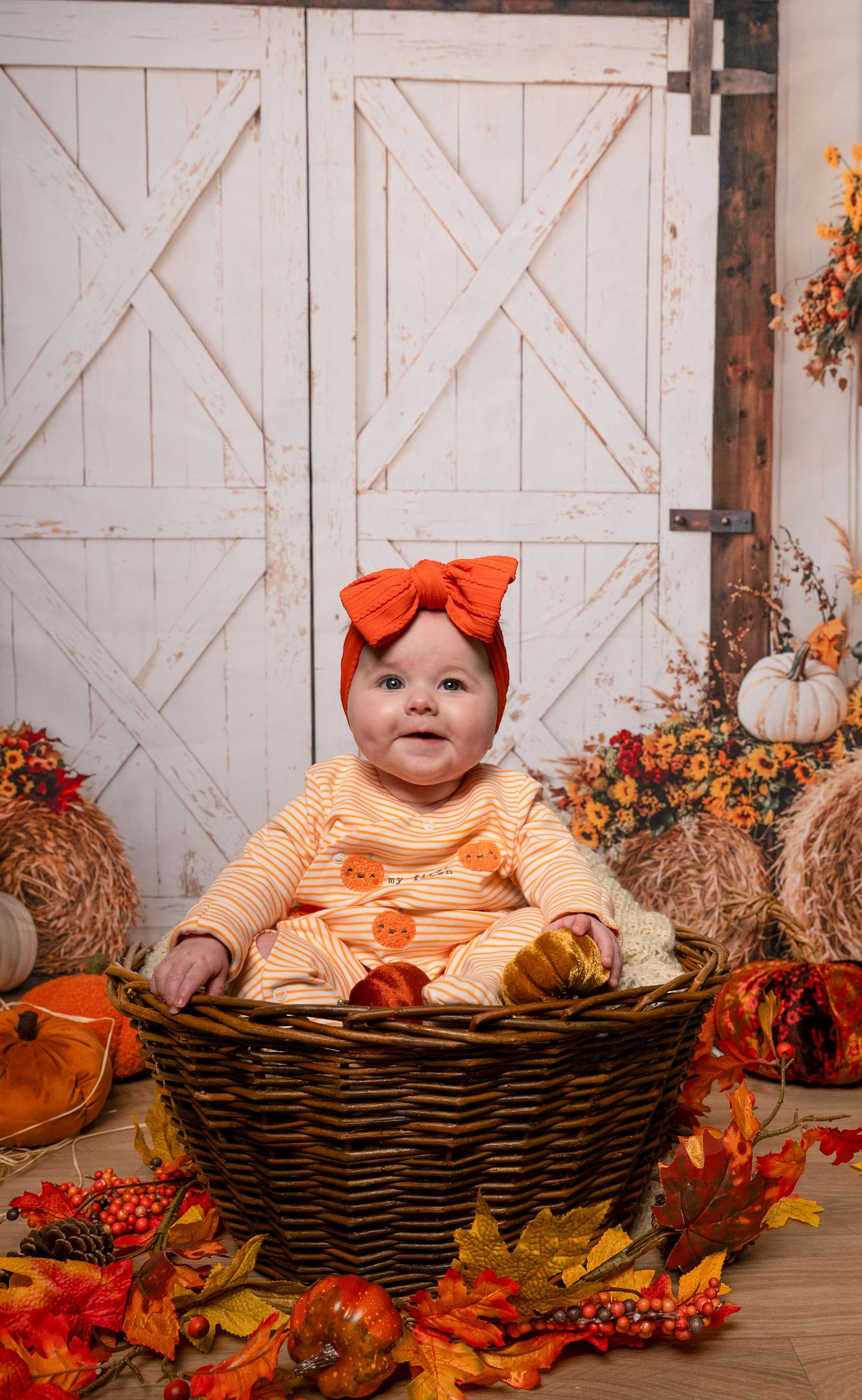 Autumn themed setting with woven basket surrounded by fall leaves and orange decor against white barn doors.