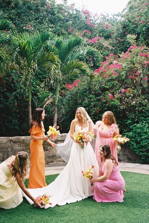 Wedding party in pink and orange dresses posing in tropical garden with palm trees and flowers.