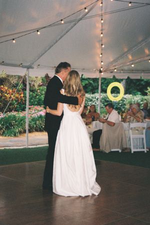 A couple shares their first dance under a tent with string lights at an outdoor wedding reception.
