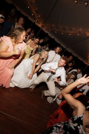 Wedding guests dancing and celebrating on wooden dance floor under tent at night.