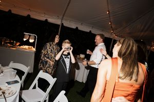 Silhouettes of wedding guests dancing and celebrating at a dimly lit reception under a tent.