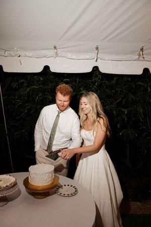 Newlyweds playfully cutting their wedding cake together at the reception.