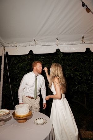 Wedding cake cutting moment at reception under white tent with string lights.