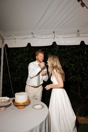 Wedding couple shares a playful moment while cutting their wedding cake under a white tent.