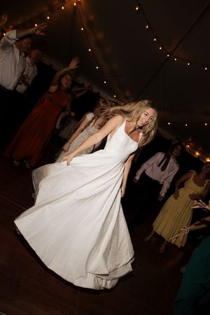 Bride twirls in her elegant white wedding dress on the dance floor under string lights.