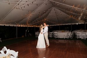 Large wedding reception tent with wooden dance floor and twinkling string lights overhead.