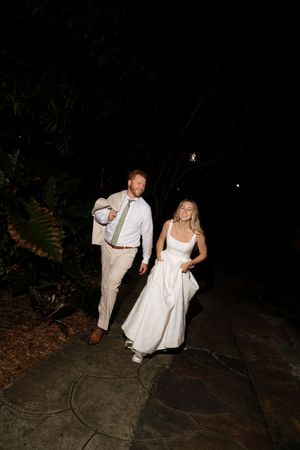 A couple in wedding attire dances playfully on a dark pathway at night.