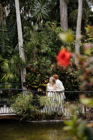 A romantic moment captured in a tropical garden with palm trees and red flowers blooming in the foreground.