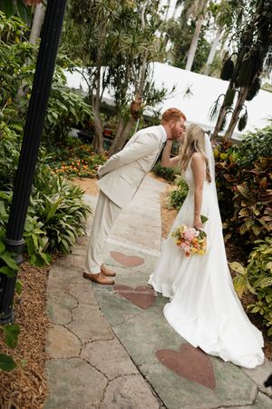 Wedding couple shares playful moments on stone pathway surrounded by tropical landscaping.