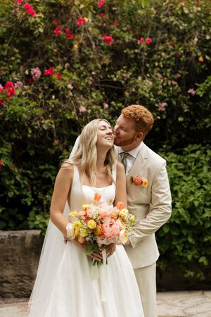 A romantic garden wedding photoshoot with coral and peach bouquet against flowering bushes.