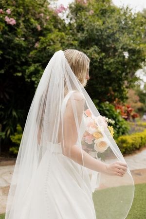 Flowing wedding veil and bouquet captured in soft natural garden lighting.