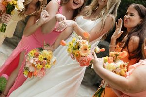 Bridesmaids in coral dresses hold vibrant peach and yellow floral bouquets at outdoor wedding.