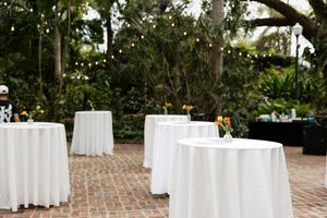 Outdoor wedding venue with white round tables and brick patio.