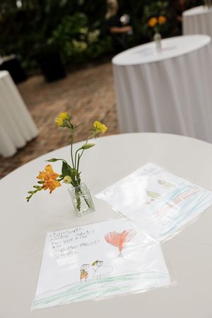 Handwritten cards and small flower arrangements on white tablecloths.