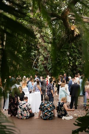 Large group of wedding guests gathered on a shaded brick patio for outdoor celebration.