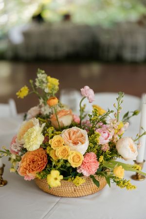 Romantic floral centerpiece with pink, yellow and peach roses arranged in a woven basket container.