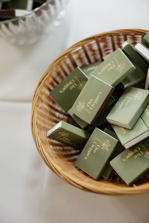 Woven basket filled with sage green wedding favor boxes on white tablecloth.