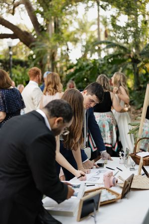 Wedding guests sign the guestbook at an elegant outdoor reception table under natural lighting.
