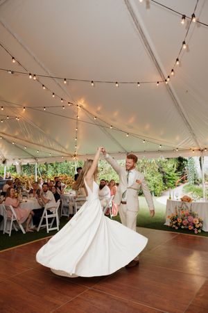 A couple spins gracefully during their first dance under a tent with string lights at their wedding reception.