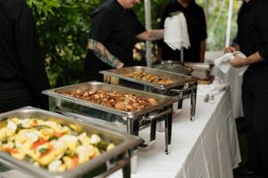 Buffet line with chafing dishes and catering staff serving food at an outdoor event.