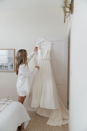 White wedding dresses displayed on hangers against a light colored wall.