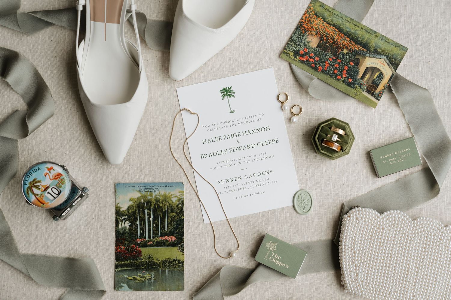 Wedding invitation suite with floral details, rings, and vintage-inspired stationery laid out on white fabric.