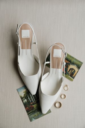 Elegant white bridal shoes arranged with vintage postcards on a light gray surface.