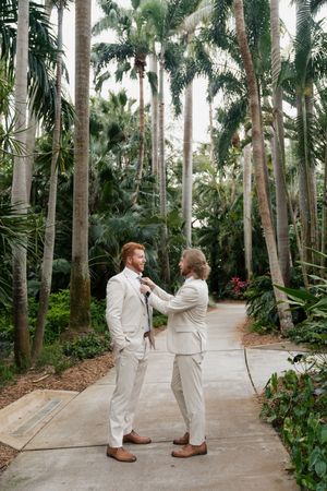 Tropical palm-lined pathway setting for a first look wedding moment in white attire.