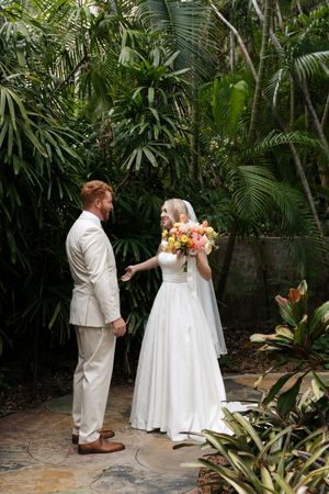 A wedding couple sharing a romantic moment in a lush tropical garden setting.