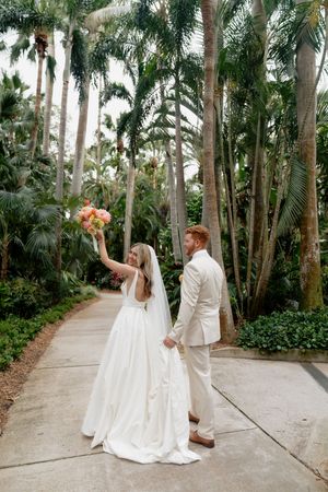 Newlyweds sharing joyful moments along a palm-lined pathway.