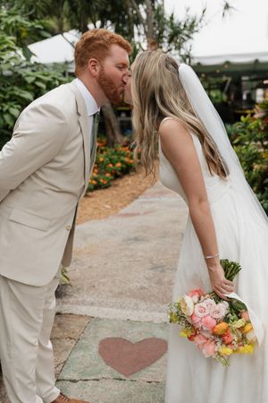 Newlyweds pose with heart shape on ground in tropical garden setting.