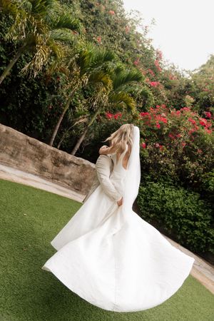 A flowing white wedding dress twirls gracefully in a lush garden setting with blooming red flowers and palm trees.