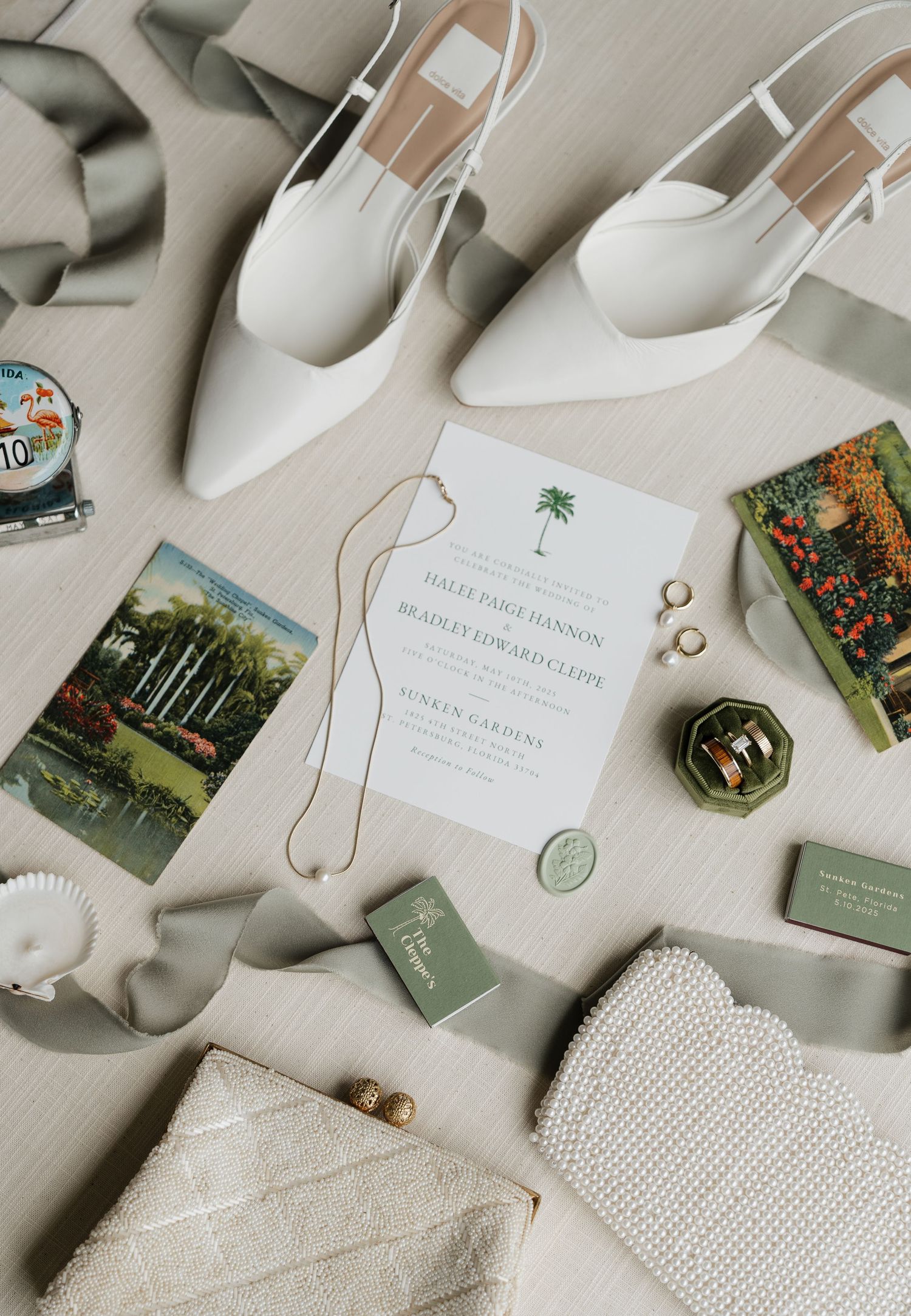 Wedding stationery and details laid out on soft gray fabric with palm tree motifs and green accents.