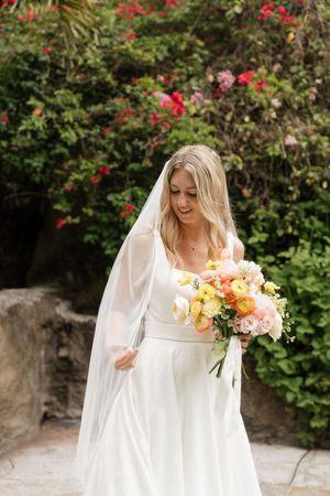 Bride in flowing white dress holds colorful bouquet in garden setting.