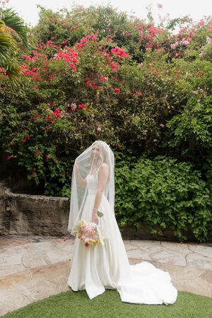 Wedding dress flowing in the breeze against flowering garden backdrop.