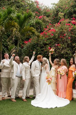Wedding party poses for photos with bridesmaids in peach dresses and groomsmen in cream suits.