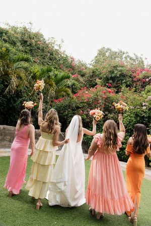 Bridesmaids in coral and peach dresses walking together on manicured lawn.