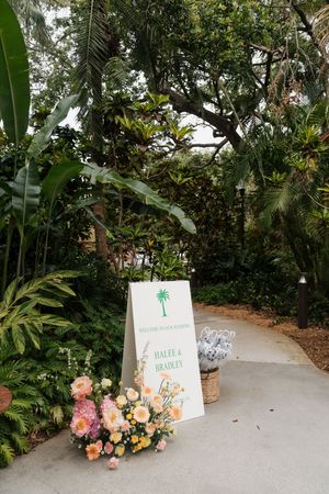 Garden pathway decorated with wedding signage and coral flower arrangements.