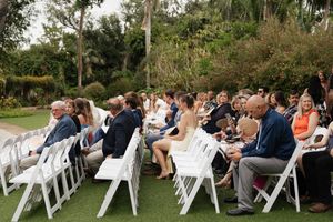 Wedding guests seated in white chairs at an outdoor ceremony venue.