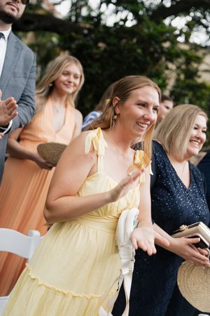 Wedding guests in colorful dresses smile and laugh during an outdoor celebration.