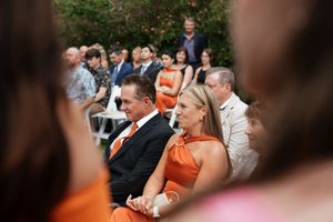 Wedding guests in formal attire seated at outdoor ceremony.