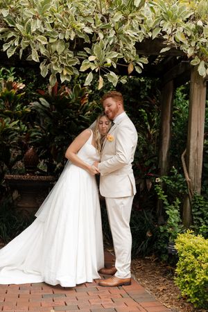 A couple poses together in a garden setting with brick pathways and lush greenery.