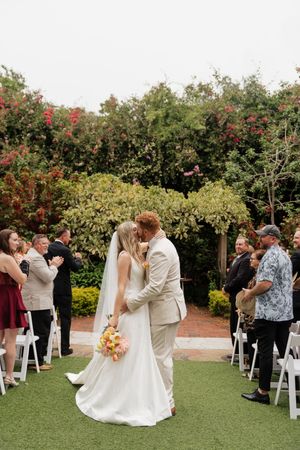 Wedding ceremony in a garden setting with white chairs and floral arrangements.
